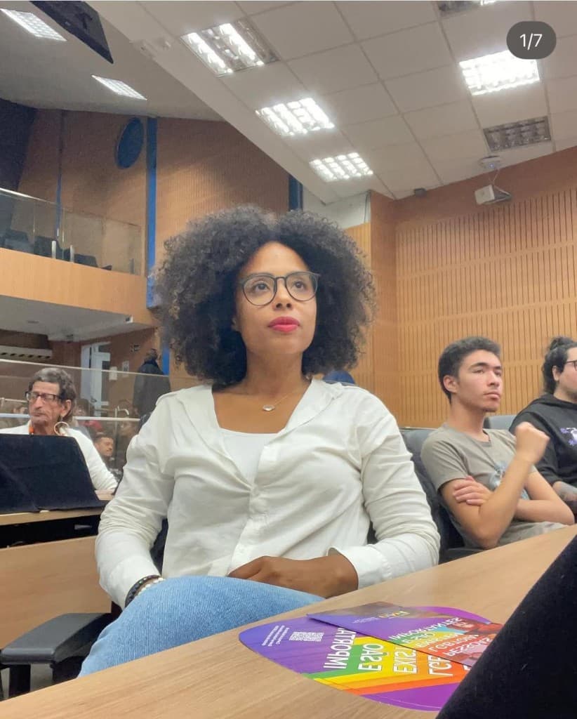 Jaque Medeiros sentada em auditório, em registro documental.