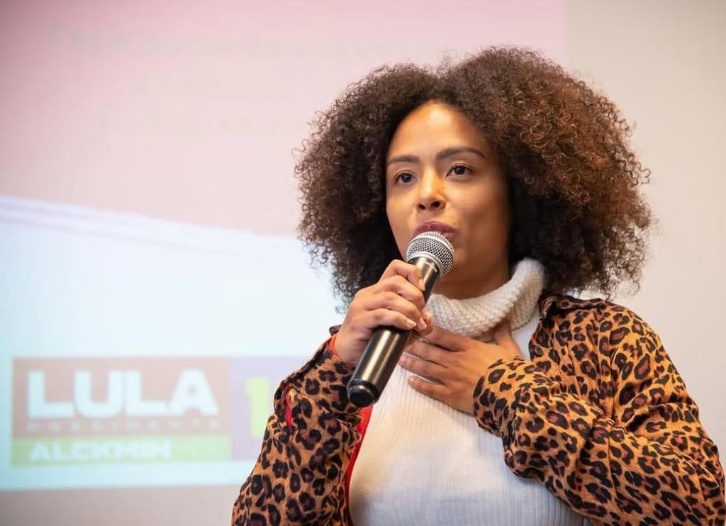 Jaque Medeiros fala ao microfone em evento público.